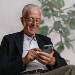 Bild eines älteren Mannes, der sitzt und auf sein Mobiltelefon schaut.