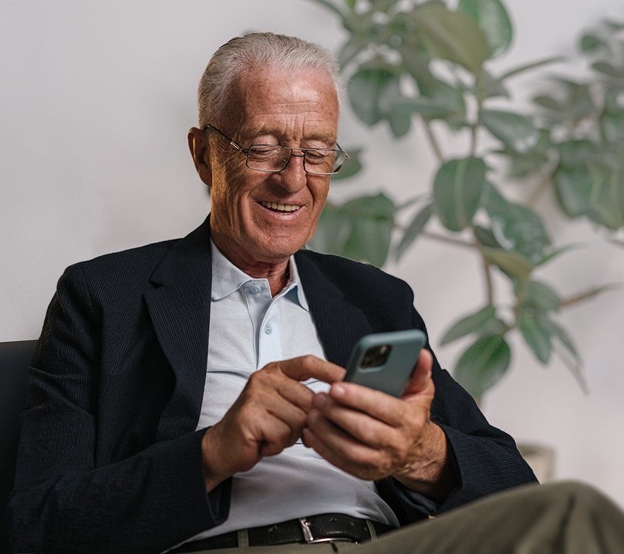 Bild eines älteren Mannes, der sitzt und auf sein Mobiltelefon schaut.
