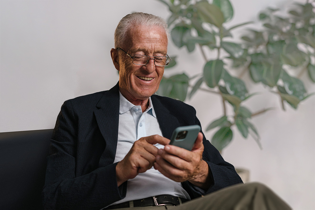 Bild eines älteren Mannes, der sitzt und auf sein Mobiltelefon schaut.